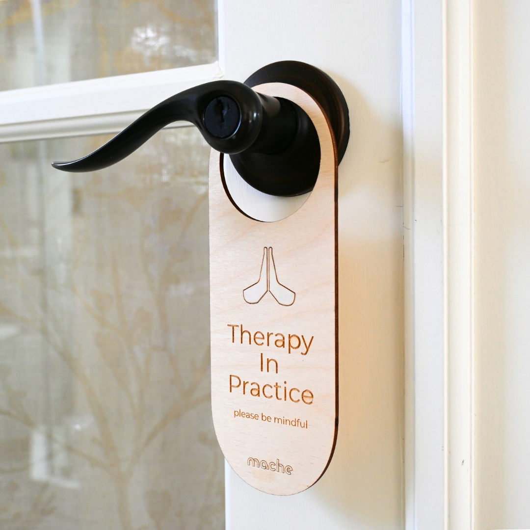 Light wood door handle hanger reading 'Therapy In Practice' on a door.