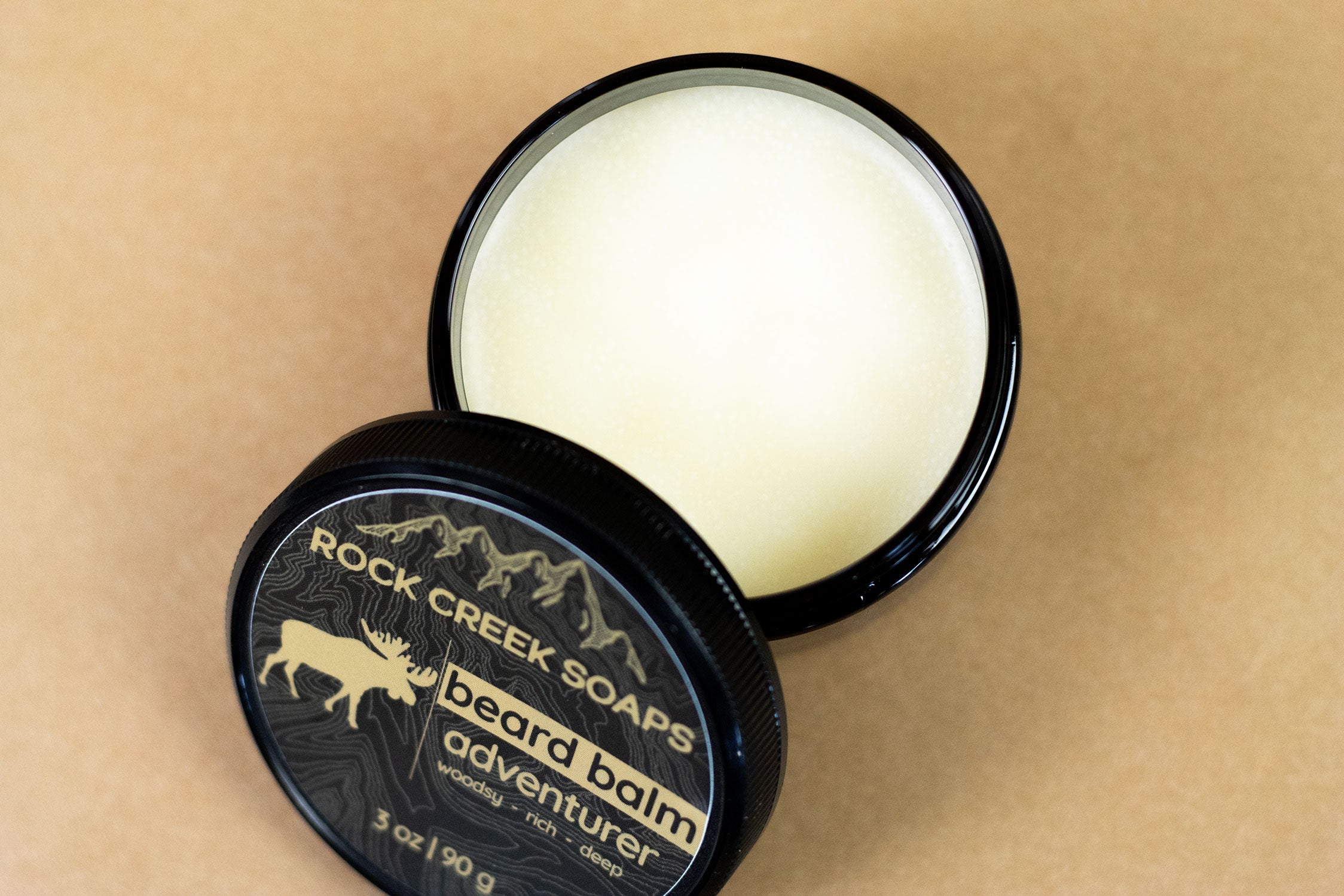 Beard balm container with lid open on a beige background