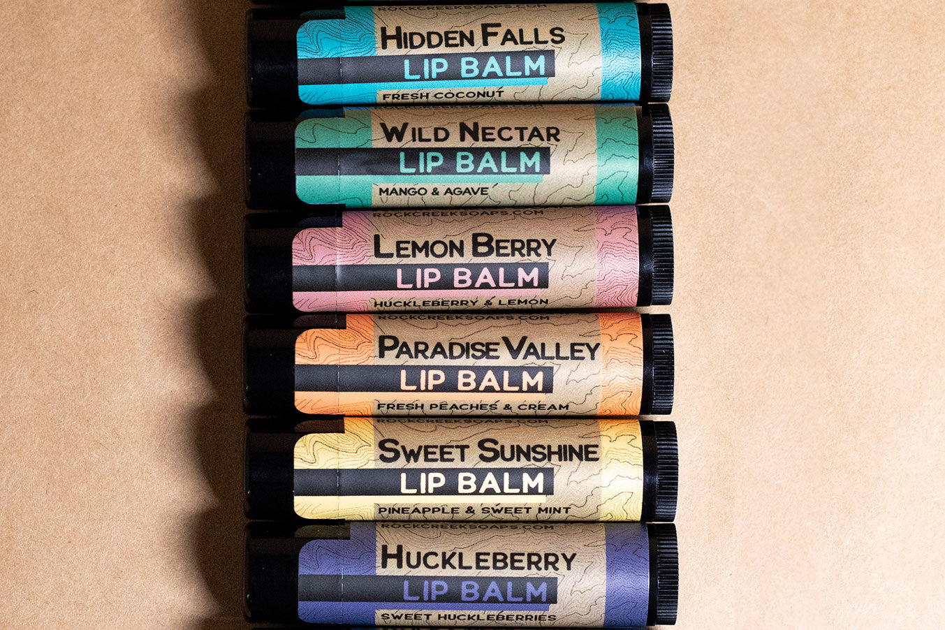 Stack of lip balm tubes with various flavors on a beige background