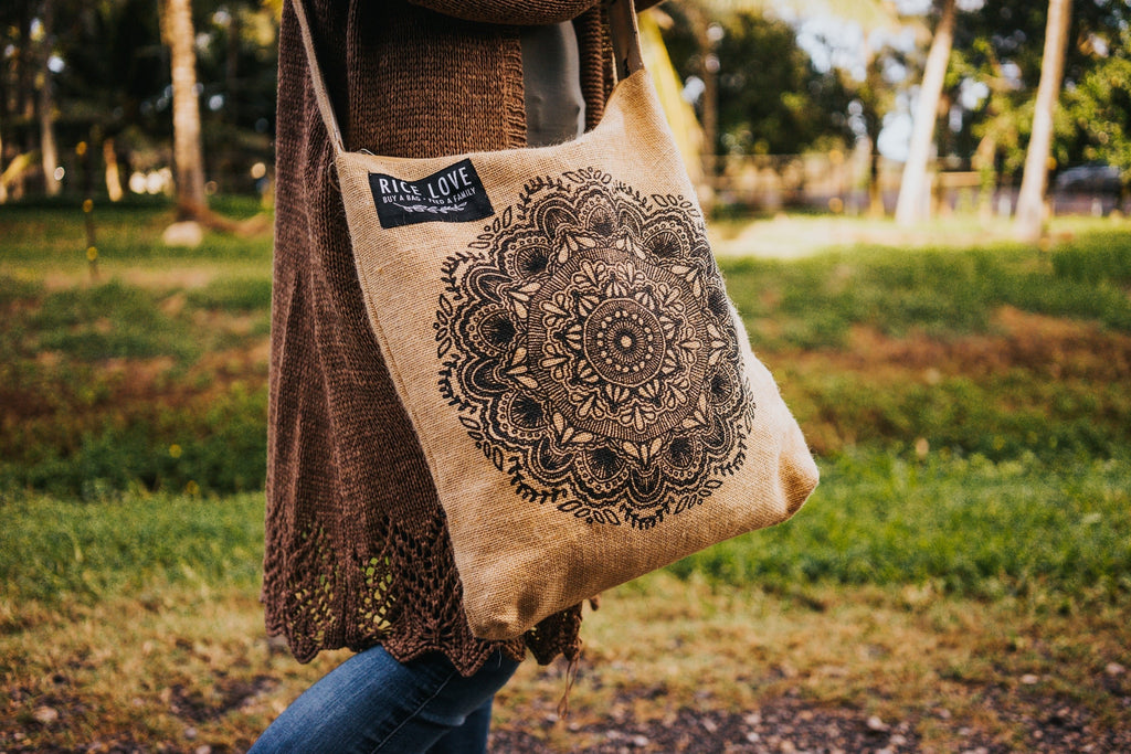 Person holding a beige tote bag with mandala design in a park setting