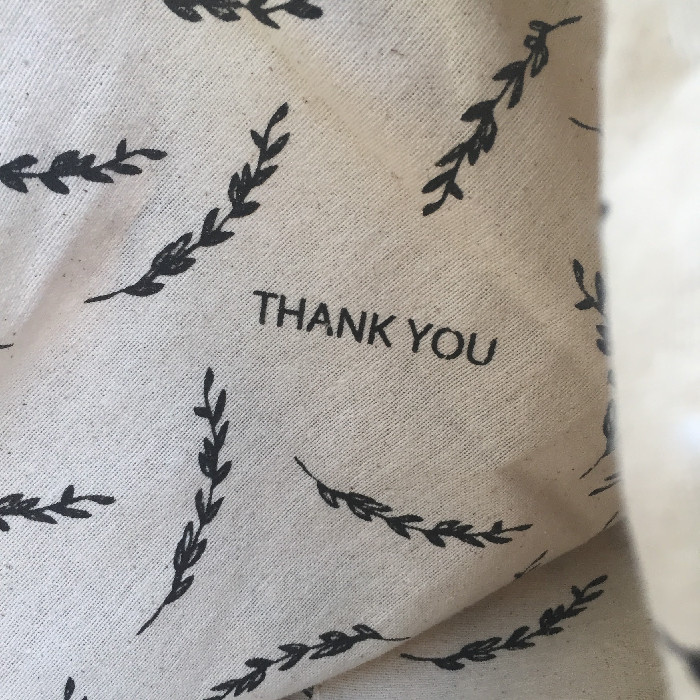 Textile with black leaf patterns and 'THANK YOU' text on a beige background