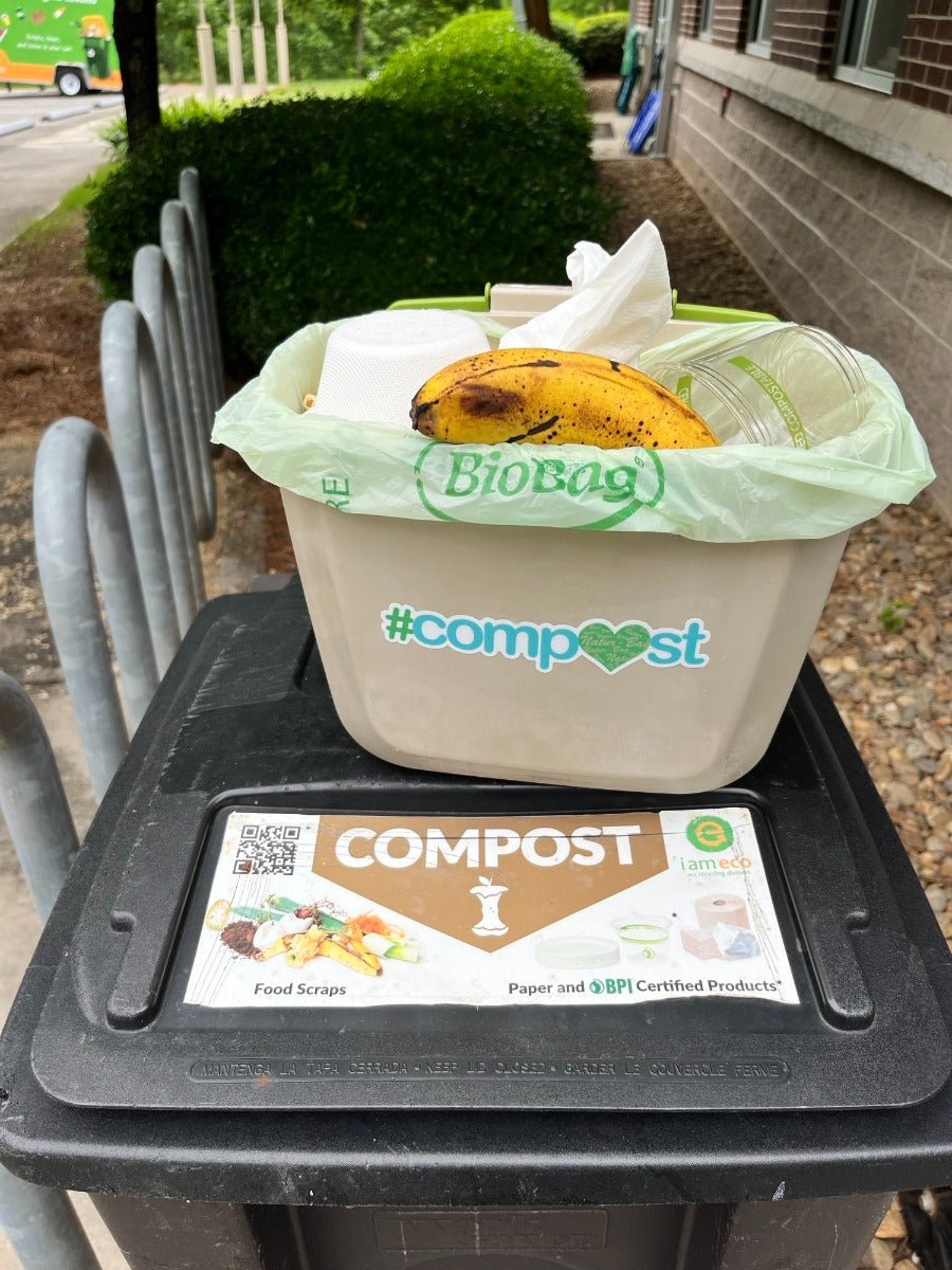Compost bag with banana peels labeled 'Biobag' in compost bin with '#compost' sticker sitting on a larger compost bin.