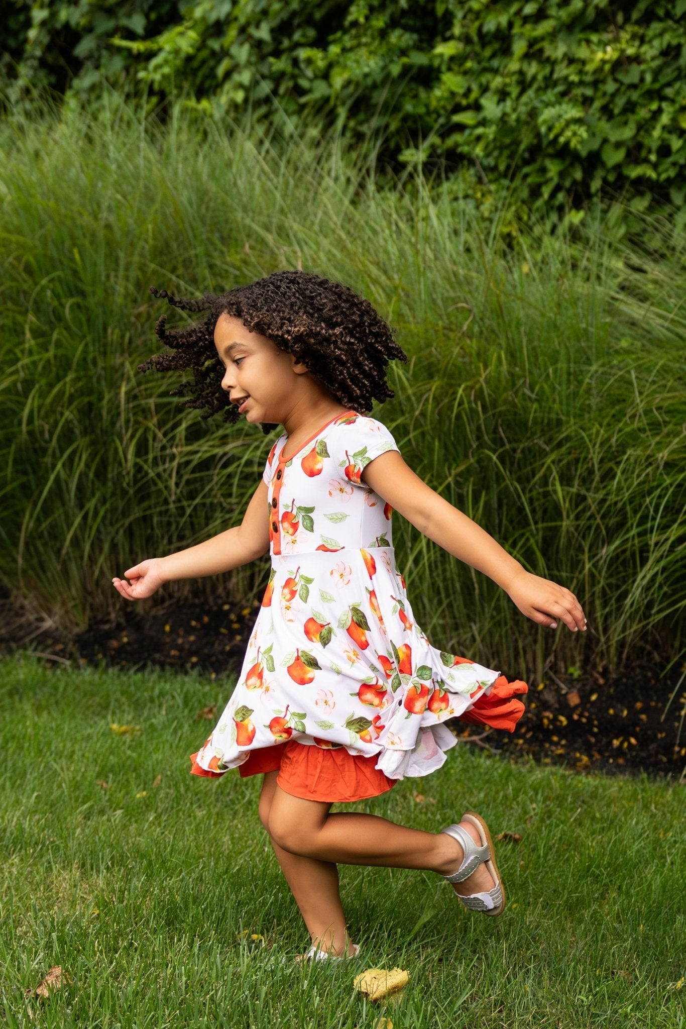 Young girl in a floral dress running on grass with greenery in the background