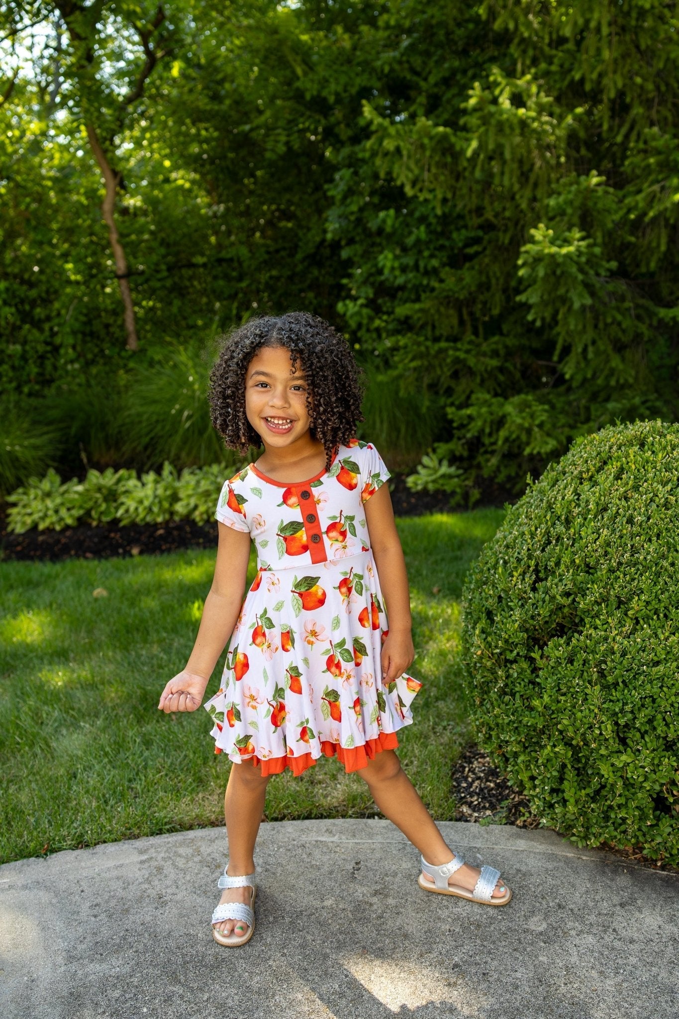 Young girl in a colorful dress standing outdoors with greenery in the background