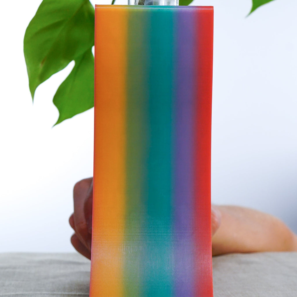 Side view of a 3D printed colorful striped planter held by a hand with a blurred background