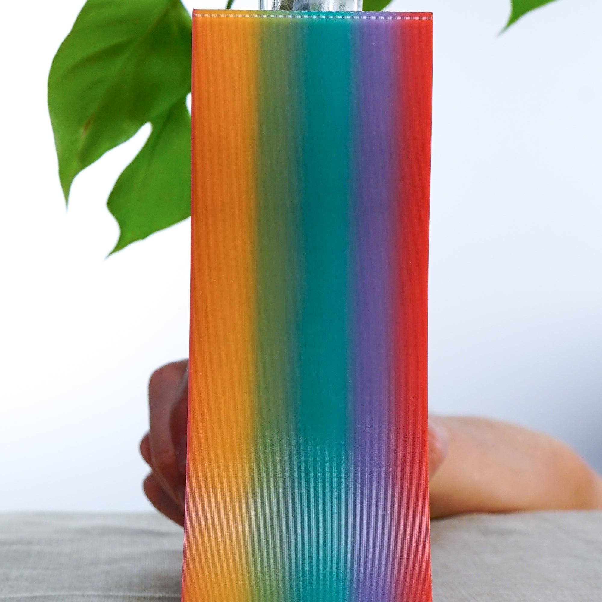 Side view of a 3D printed colorful striped planter held by a hand with a blurred background