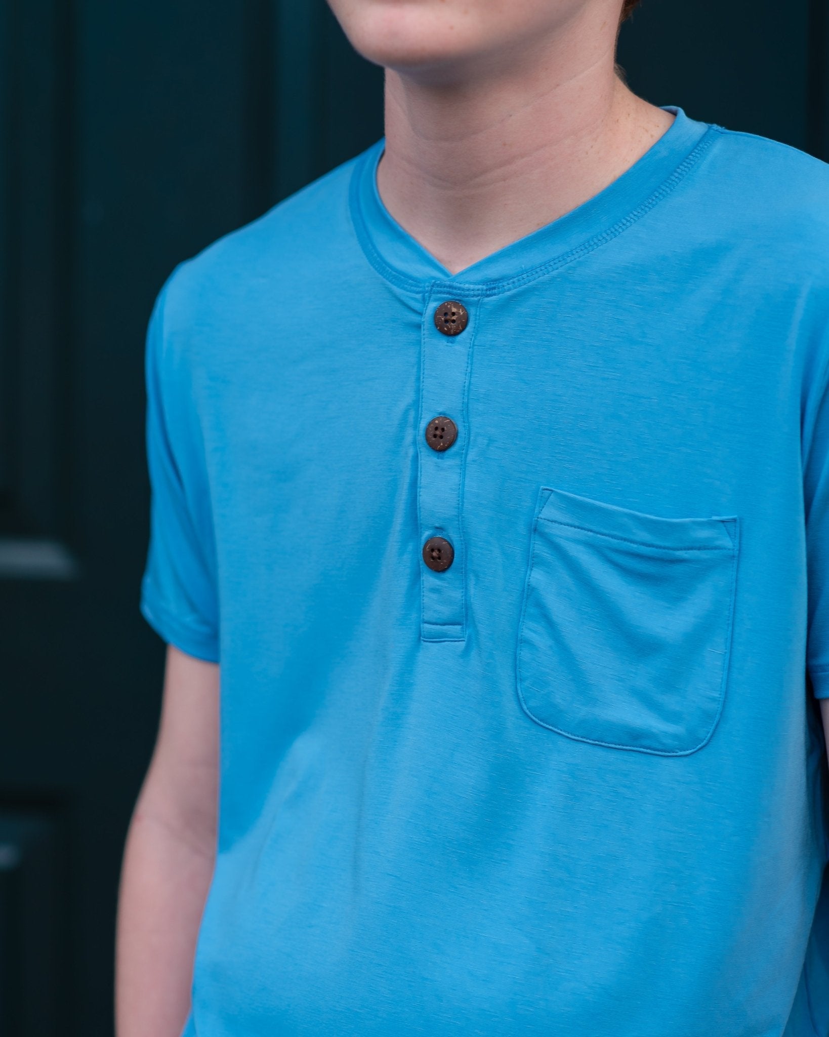 Person wearing a blue henley shirt with brown buttons on a dark background