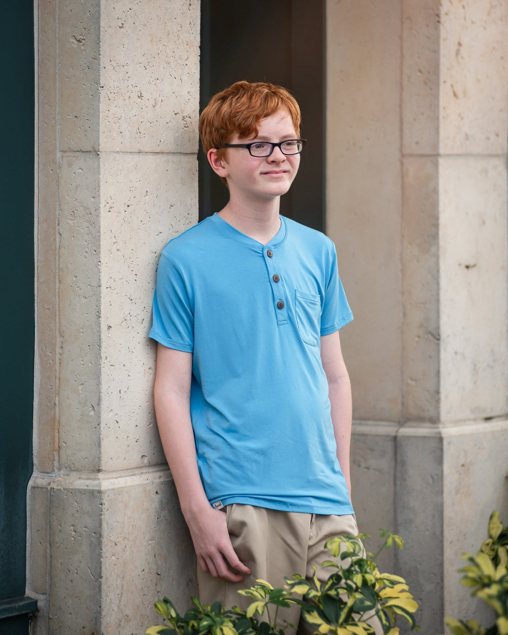 Person wearing a blue shirt standing against a stone wall.