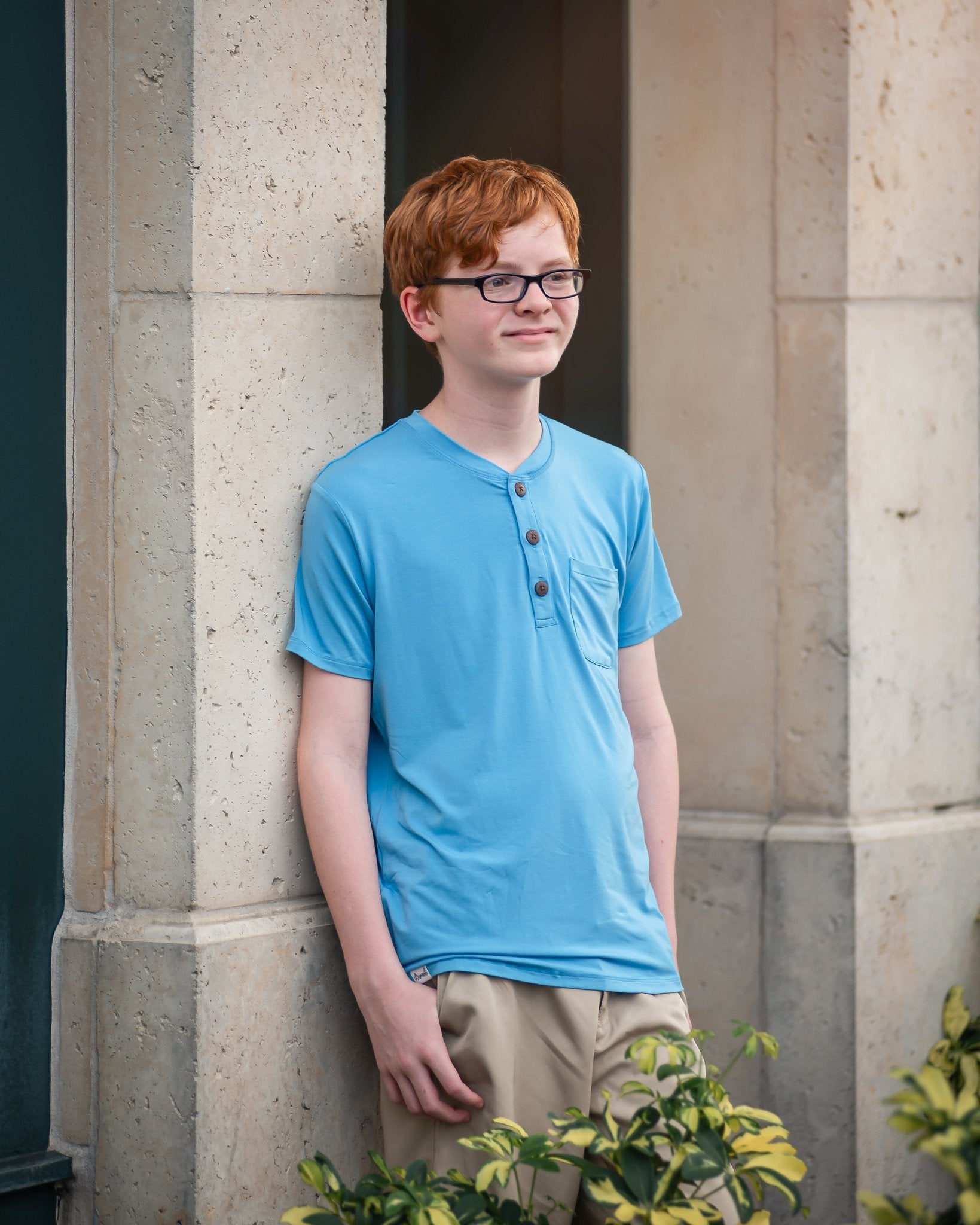Person wearing a blue shirt standing against a stone wall.