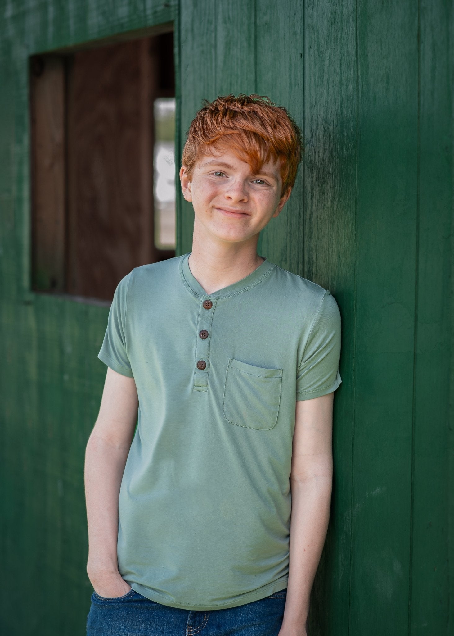 Young boy with red hair wearing a green shirt against a green wall.