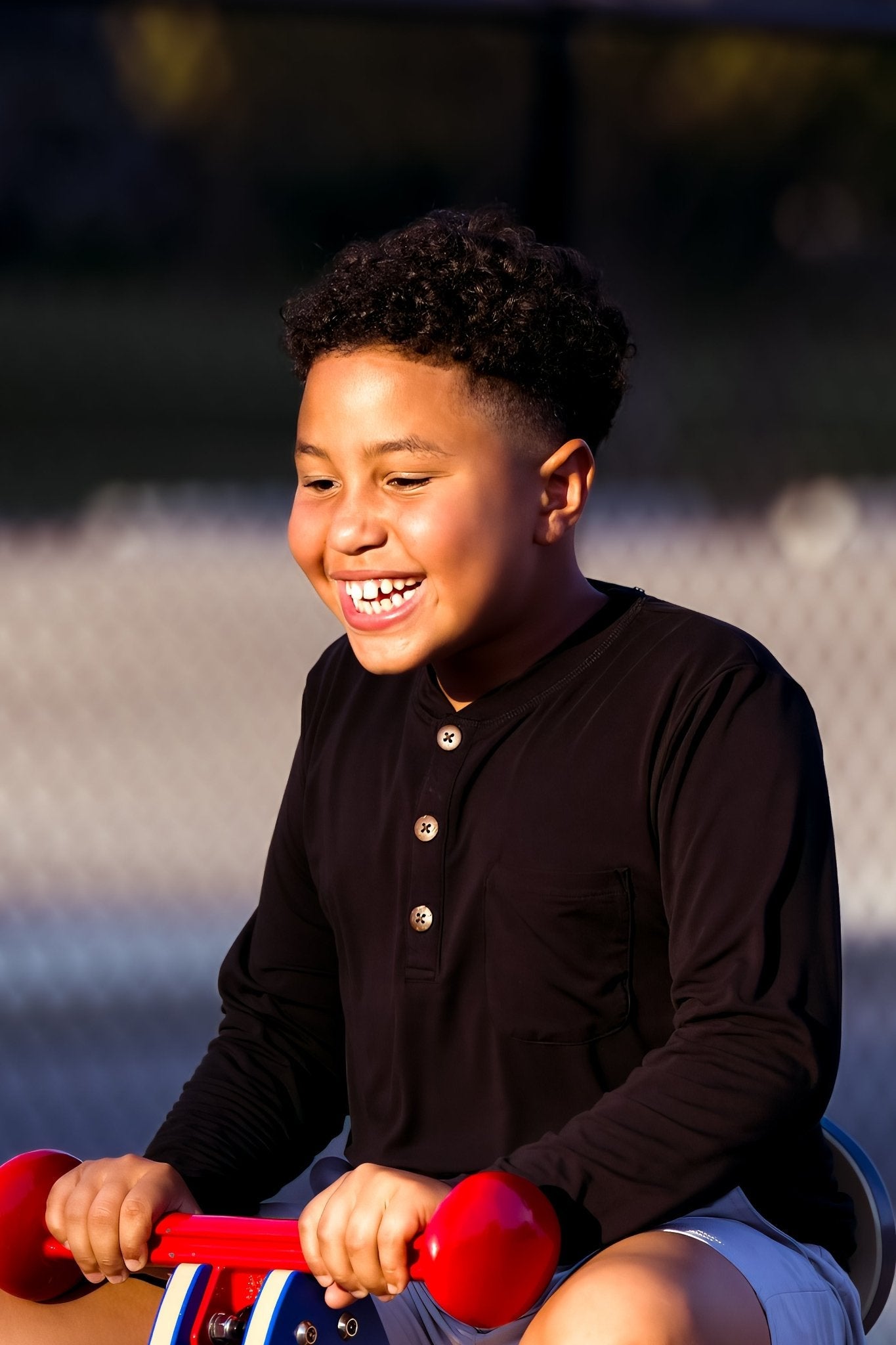 Child in a black shirt sitting on a red toy bike with a blurred background