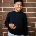 Young boy wearing a black long-sleeve shirt against a brick wall