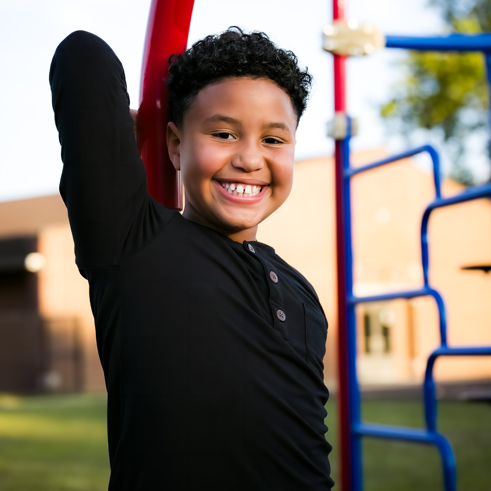 Child in a black shirt standing on a playground with a smile