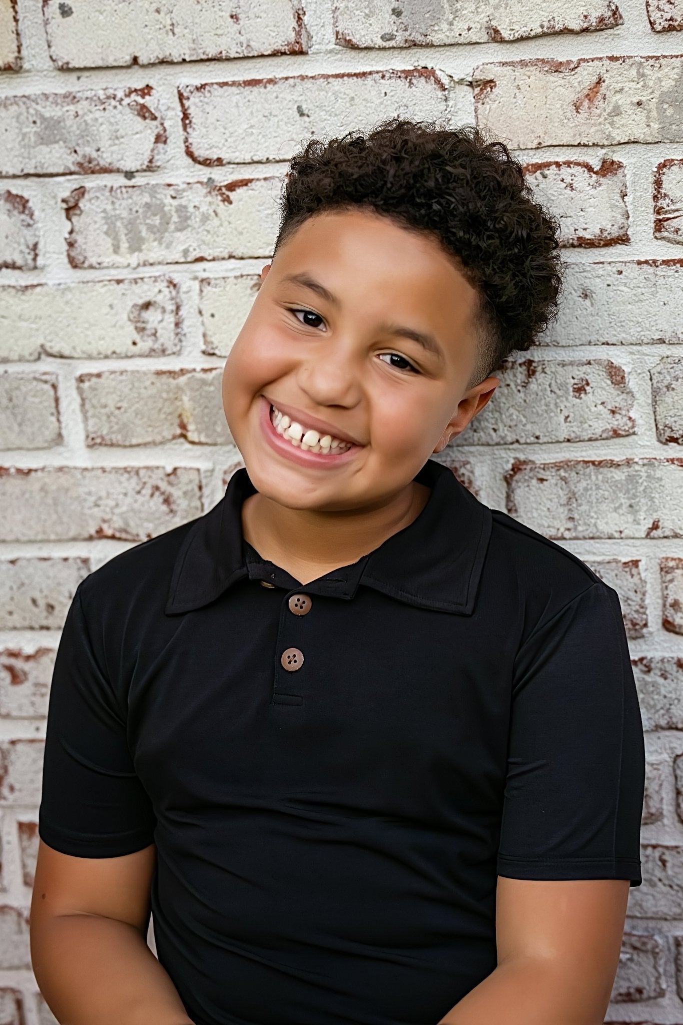 Child wearing a black polo shirt against a brick wall