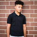 Person wearing a black polo shirt against a brick wall