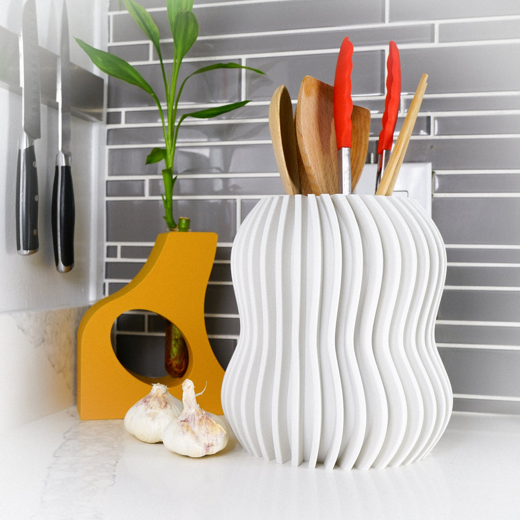 White wavy-patterned cadre with kitchen utensils on a countertop with a tiled wall background