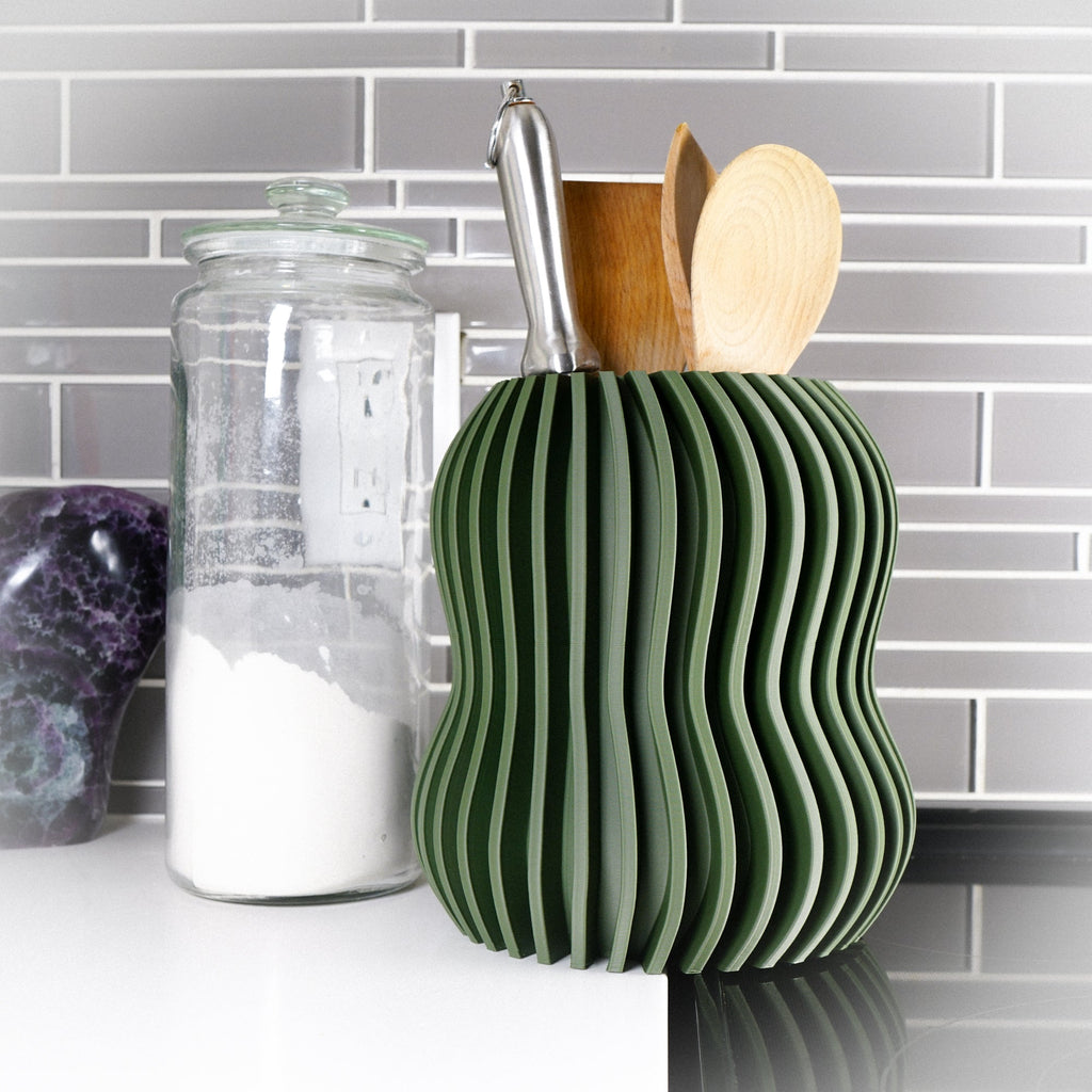 Green wavy kitchen utensil holder with wooden spoons and a metal ladle on a kitchen counter.