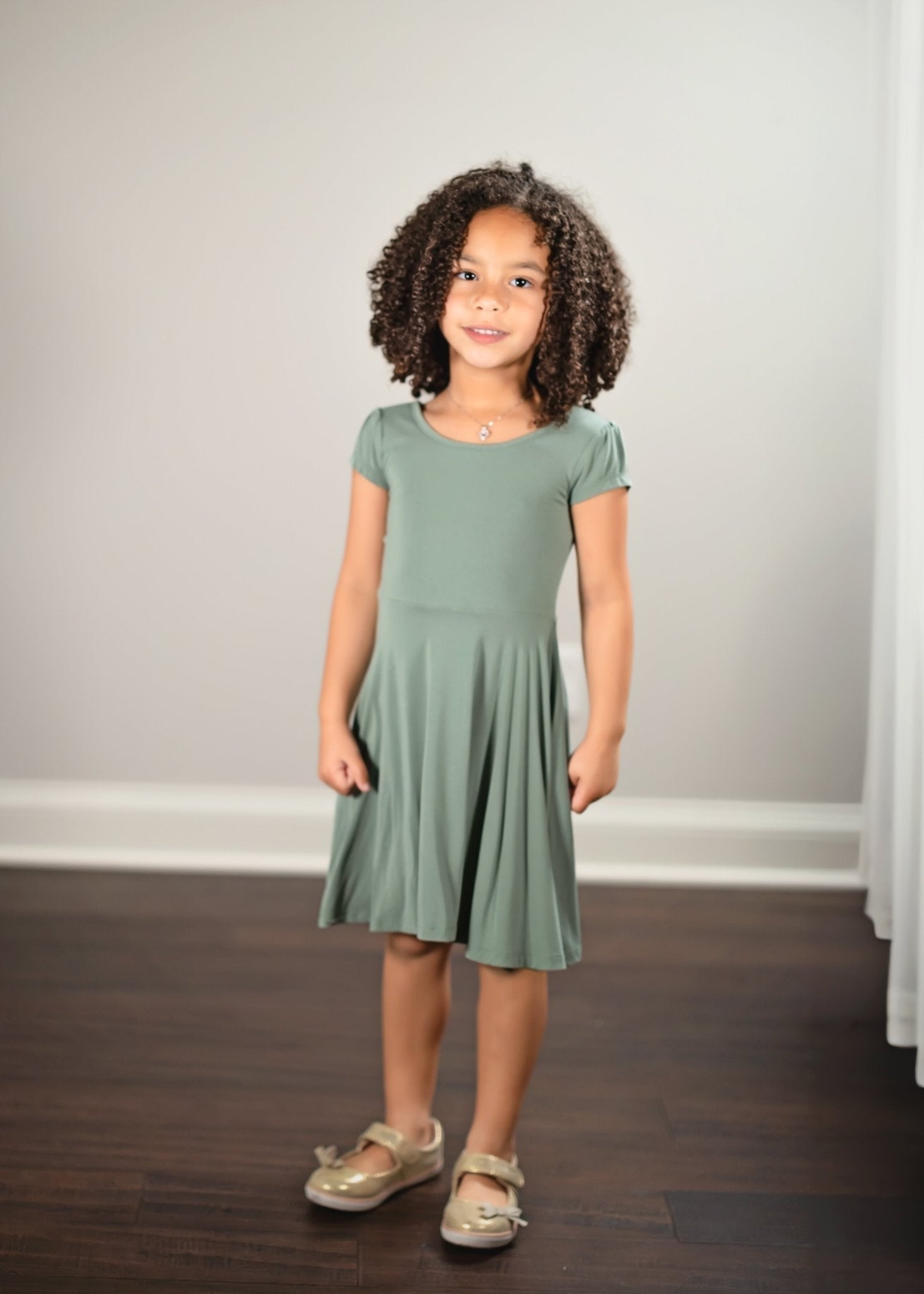Young girl wearing a green dress standing against a plain background