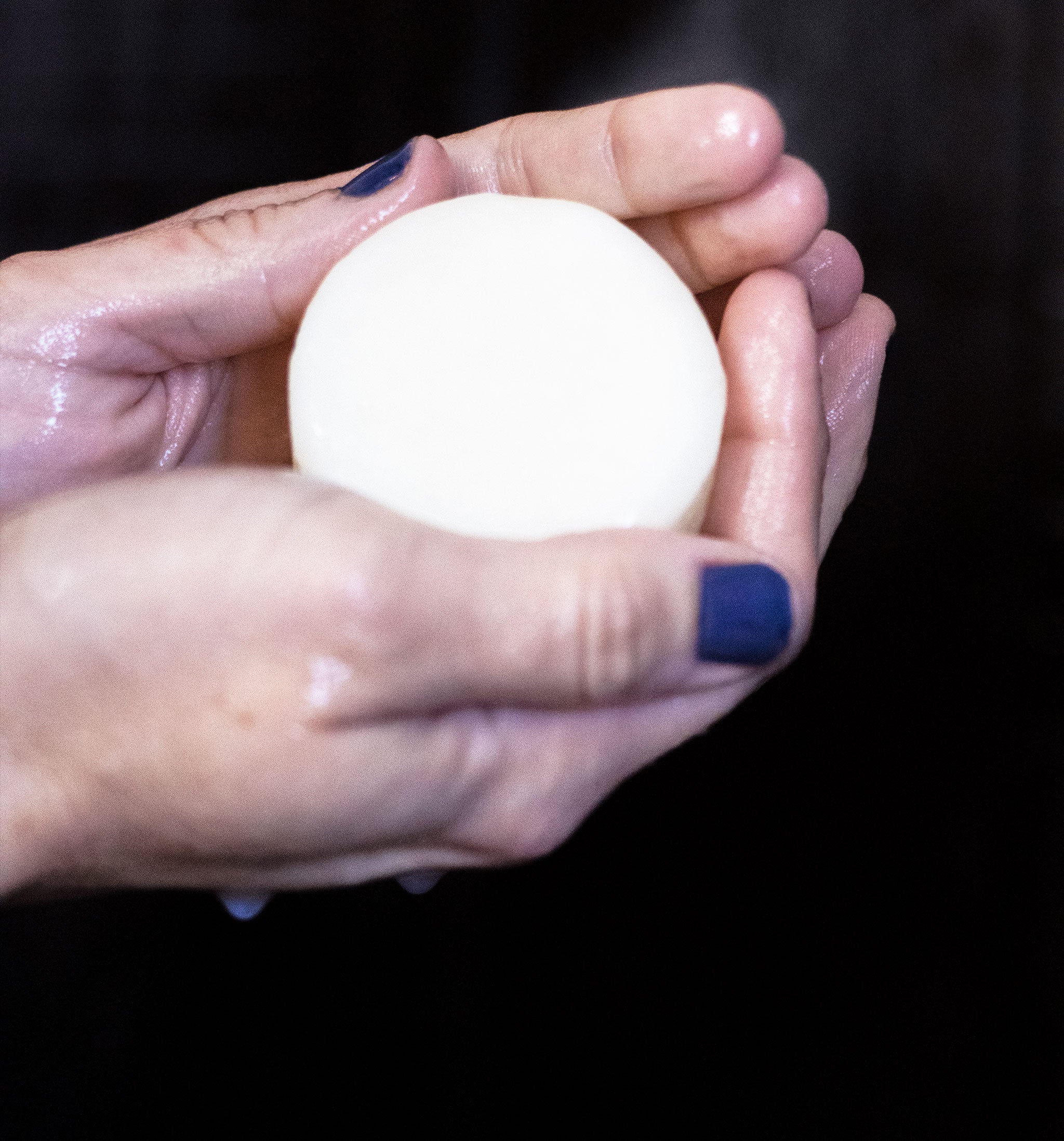 Hand holding a round hair conditioner bar against a black background