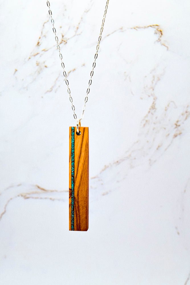 Necklace with a wooden pendant with vertical stone inlay on a marble background