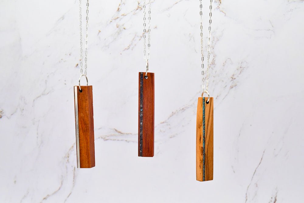 Three wooden pendant necklaces with vertical stone inlays on a marble background