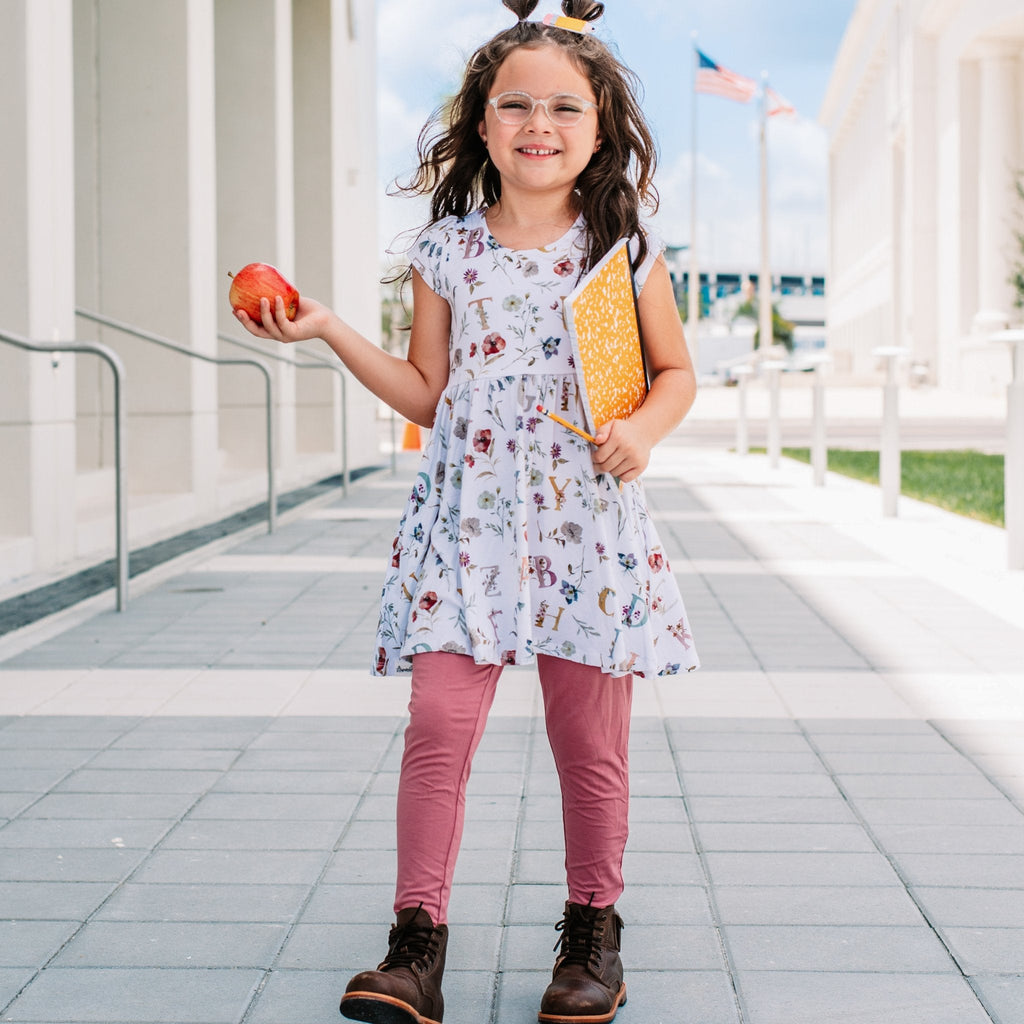 Young girl in a floral dress holding an apple and a yellow book outdoors.