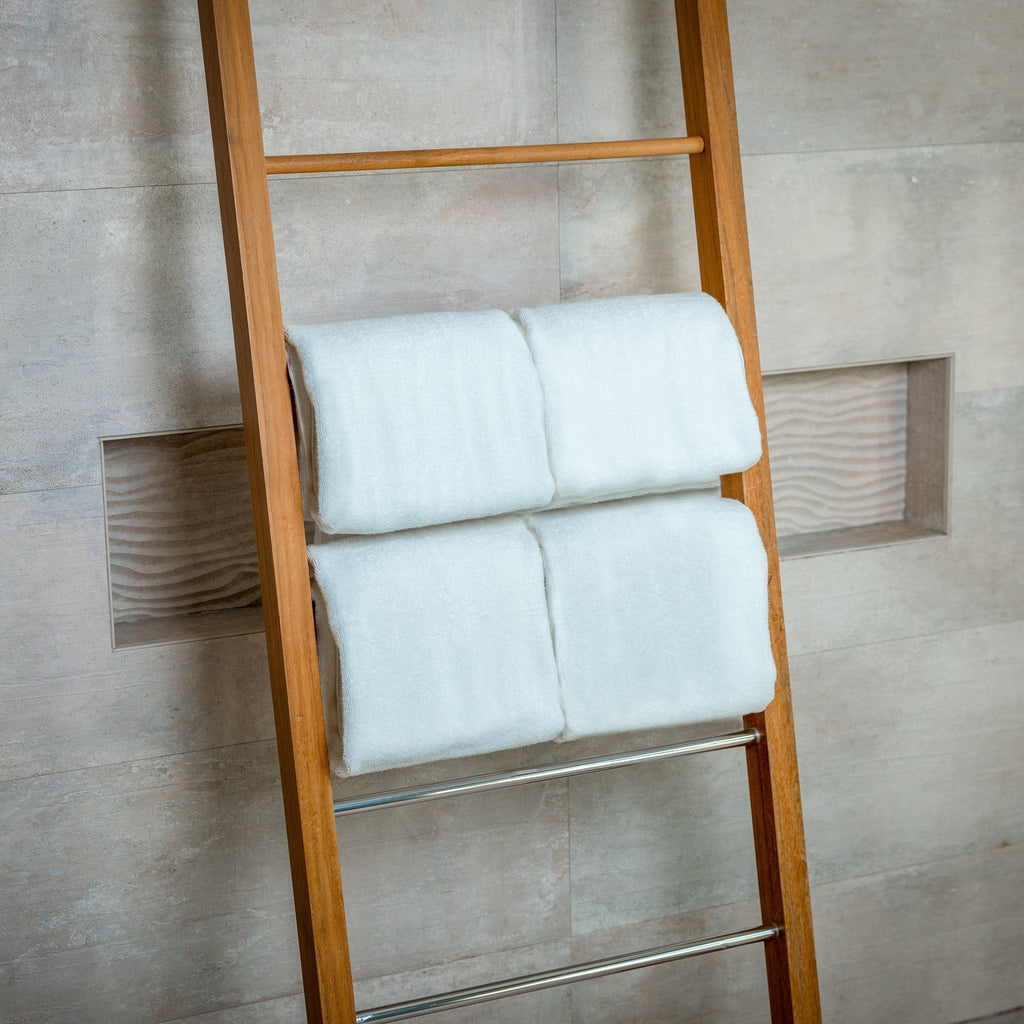 Wooden towel ladder with white towels against a tiled wall.