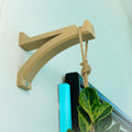 Beige metal bracket holding a hanging planter on a light blue wall.