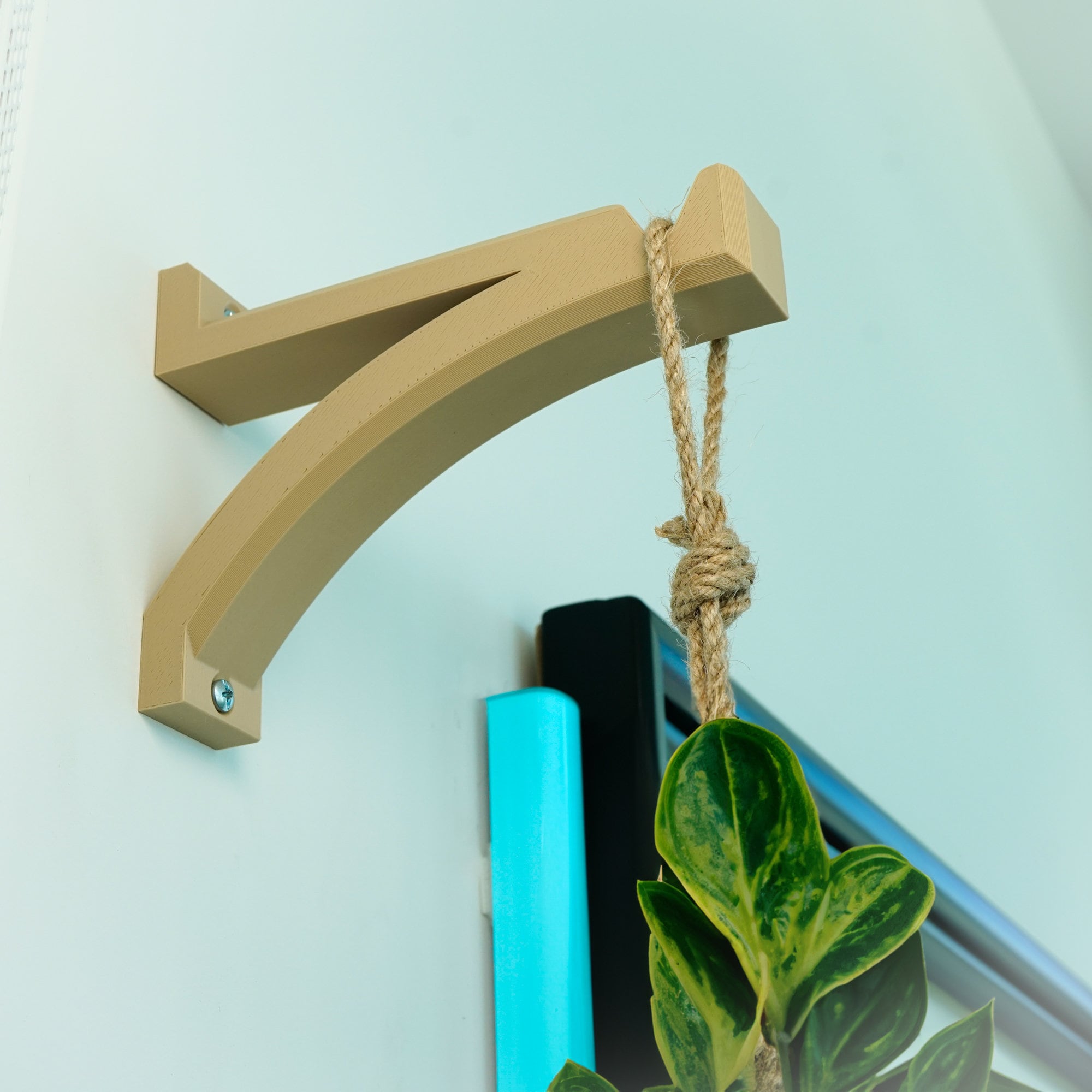 Beige metal bracket holding a hanging planter on a light blue wall.