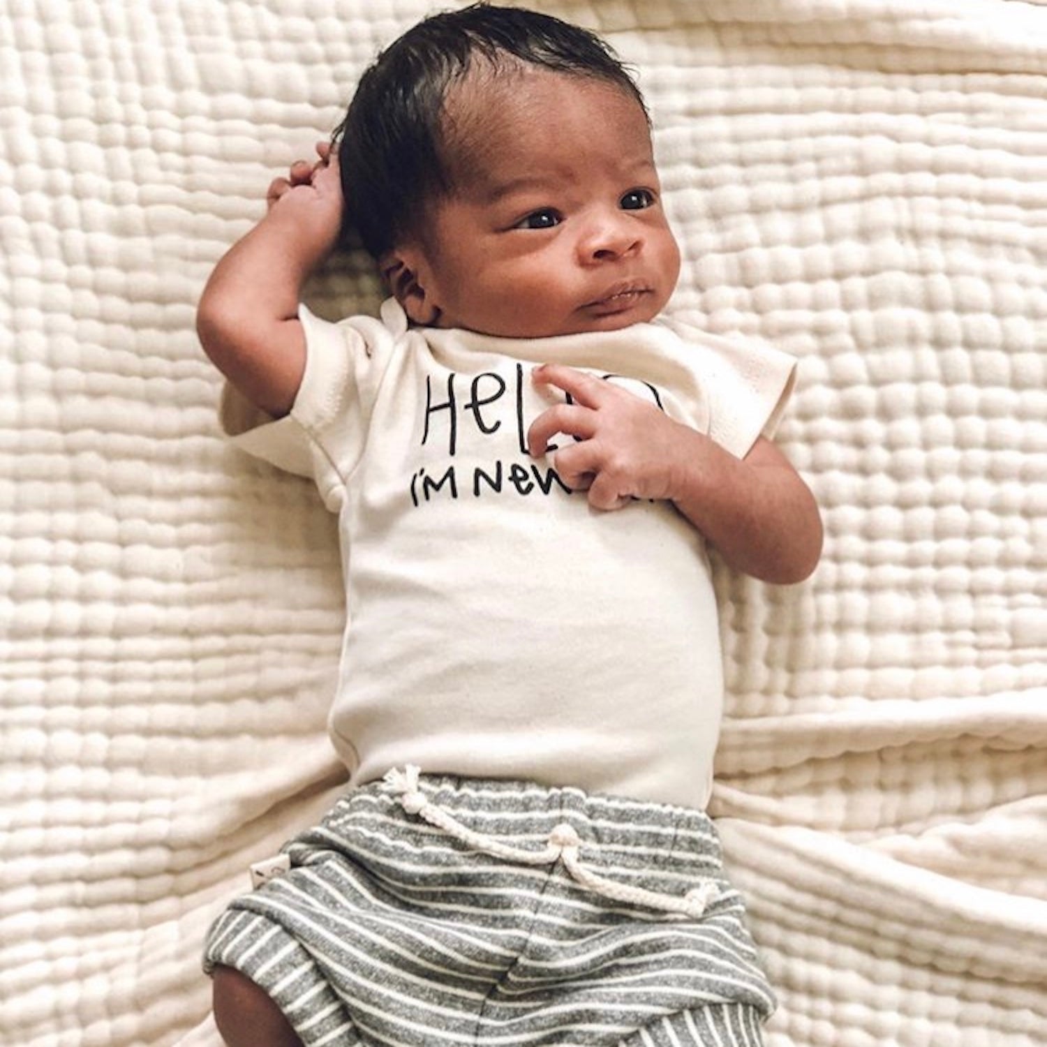 Newborn baby wearing a 'Hello, I'm New' onesie on a textured blanket