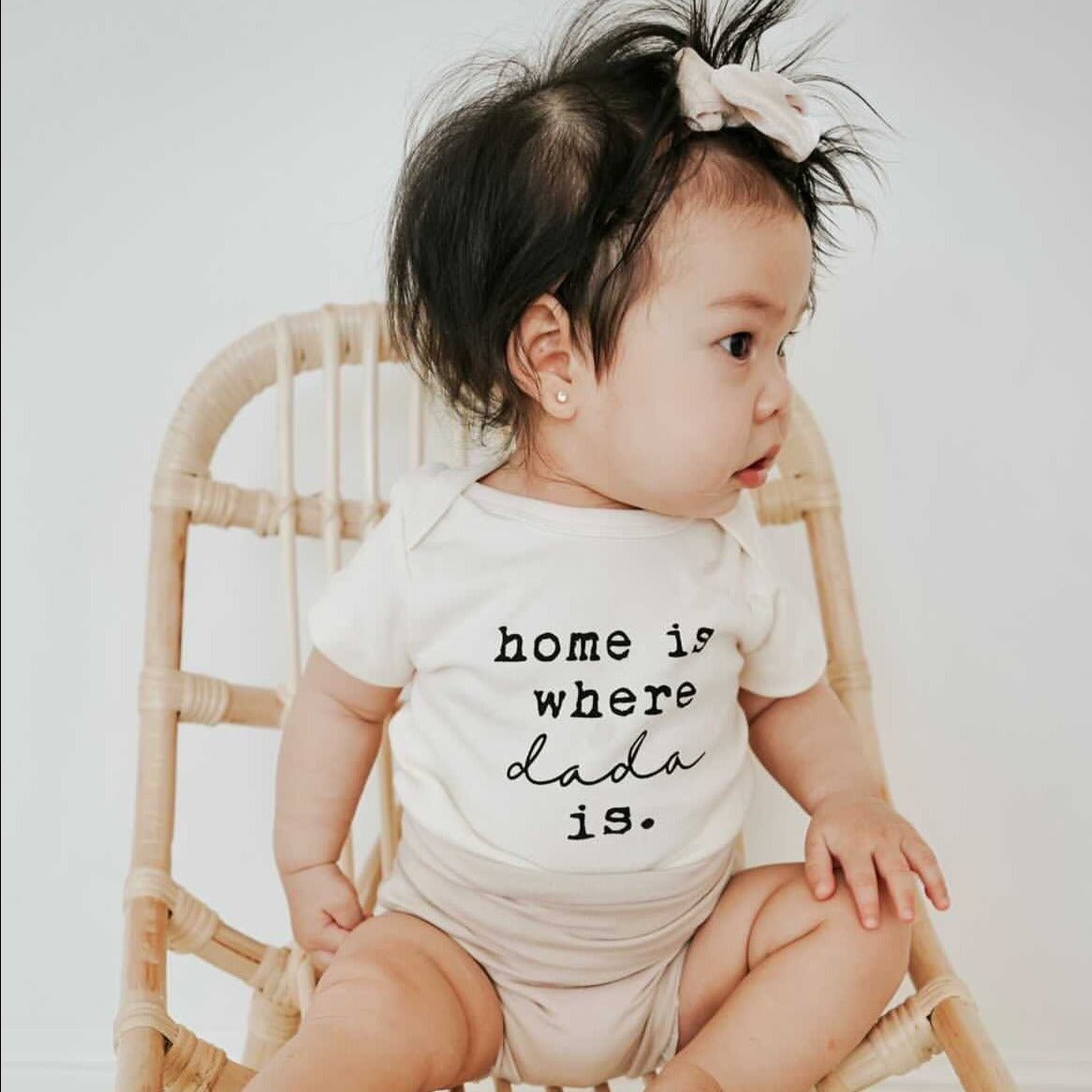 Baby wearing a onesie with 'home is where dada is' text, sitting on a chair.