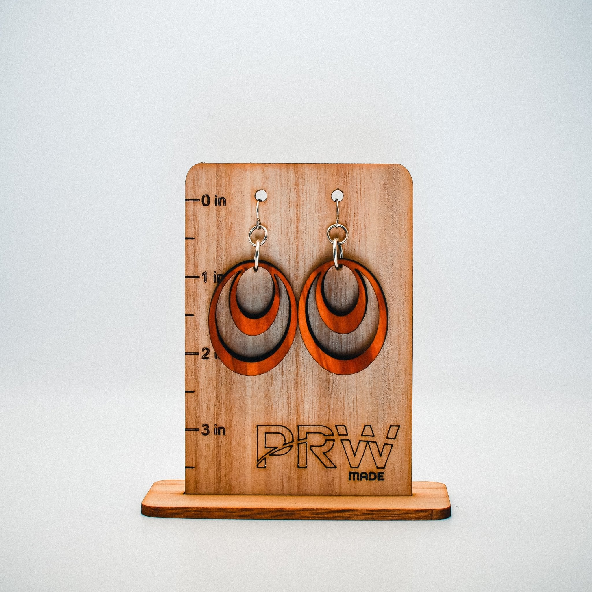 Wooden earring display with 'PRW' branding on a white background