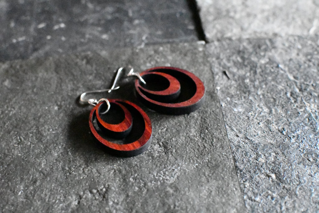 Black and red circular earrings on a gray stone surface