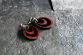 Black and red circular earrings on a gray stone surface
