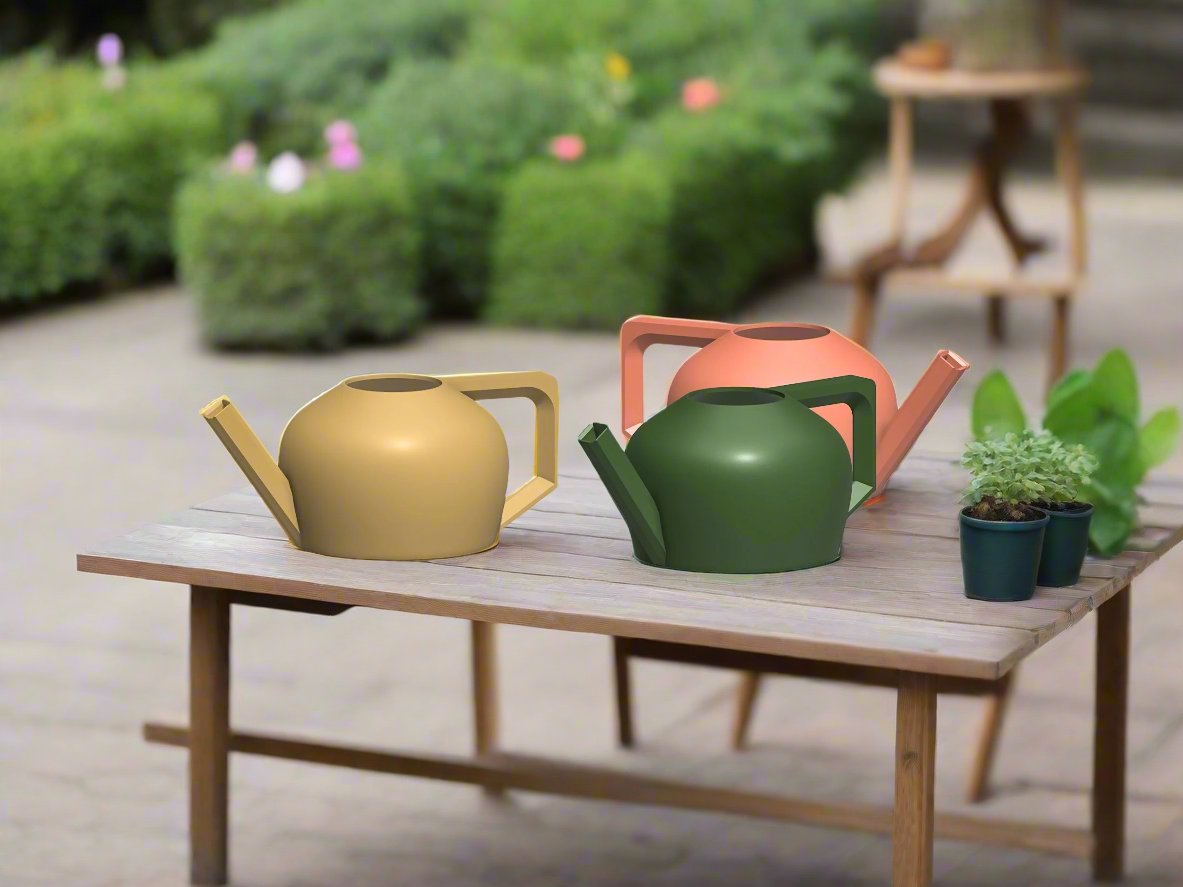 Three colorful watering cans on a wooden table with plants in the background