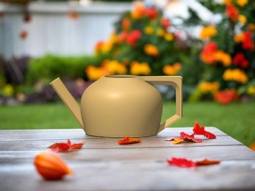 Beige watering can on a wooden table with flowers in the background
