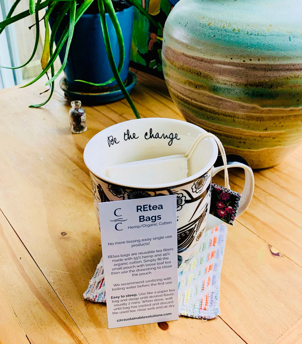 Mug with tea bags and a card on a wooden surface with plants in the background
