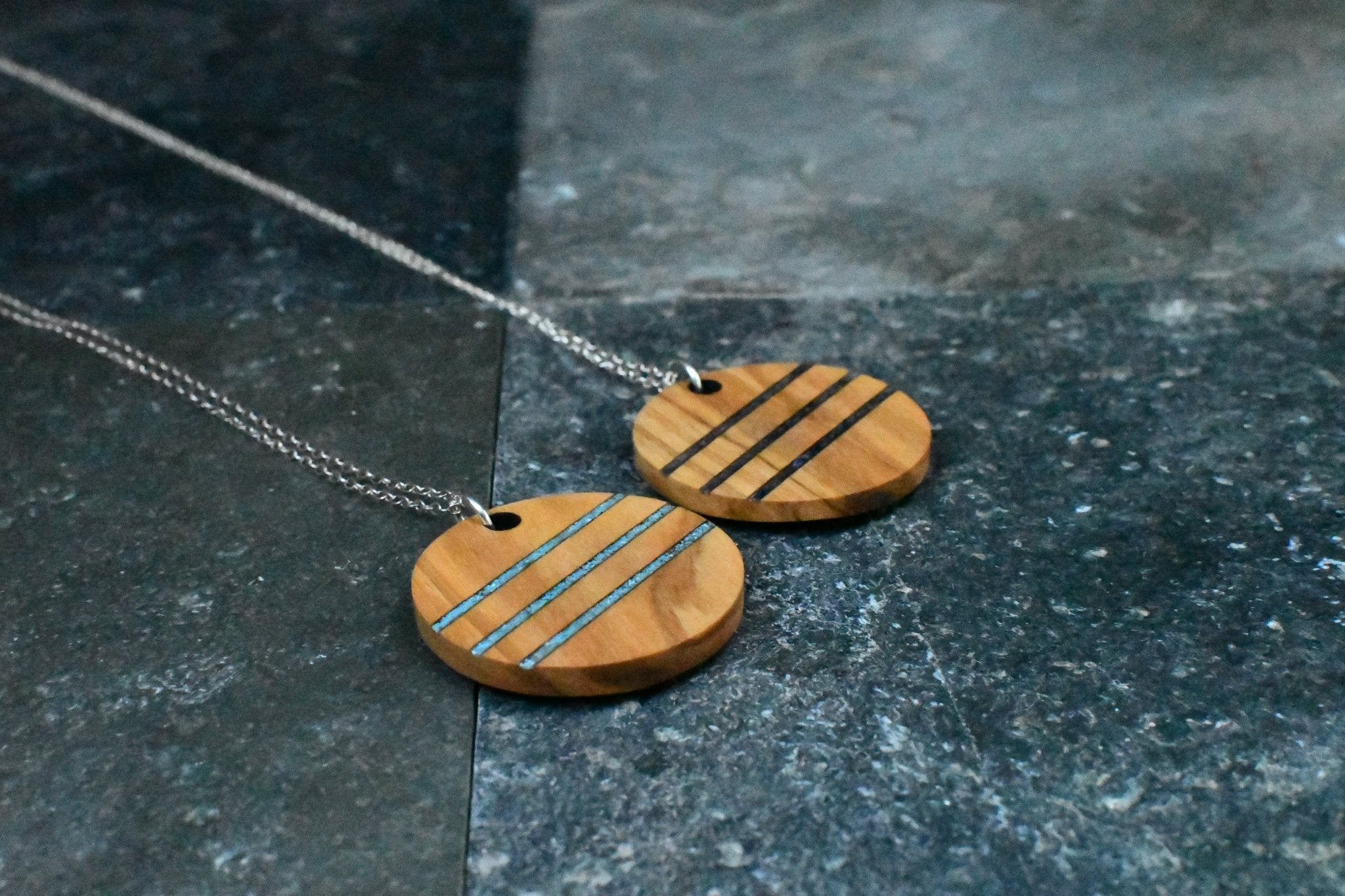 2 wooden pendant necklaces with blue and black inlay on a dark surface