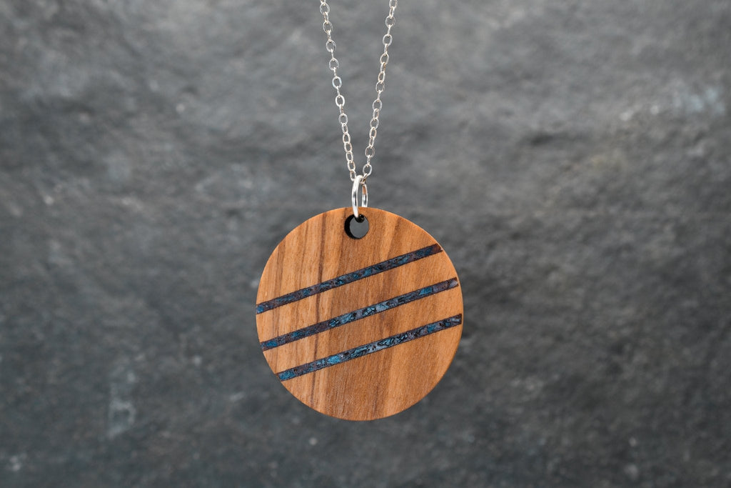 Wooden pendant with black stripes on a chain against a gray background