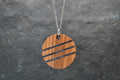 Wooden pendant with black stripes on a chain against a gray background