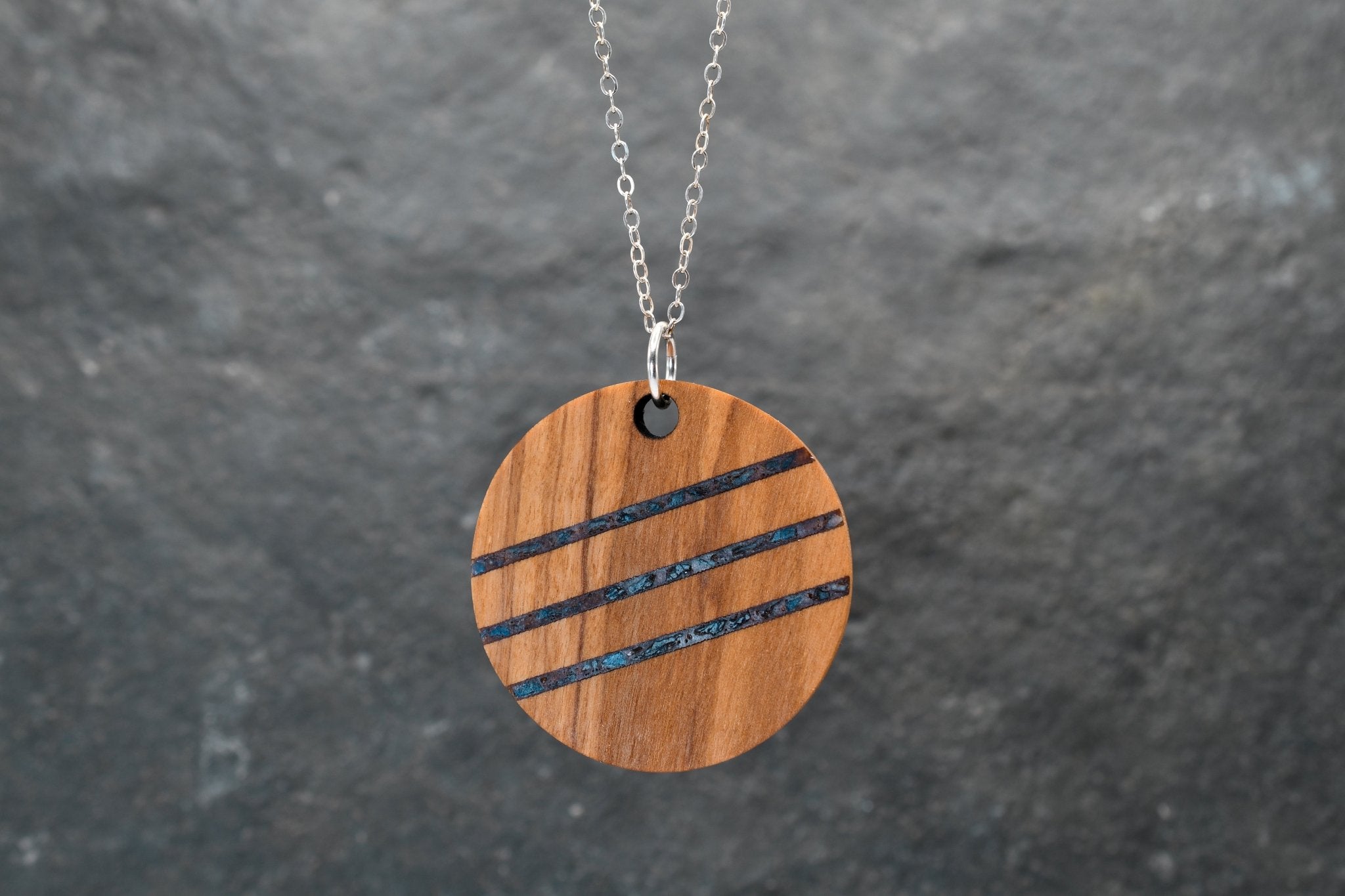 Wooden pendant with black stripes on a chain against a gray background