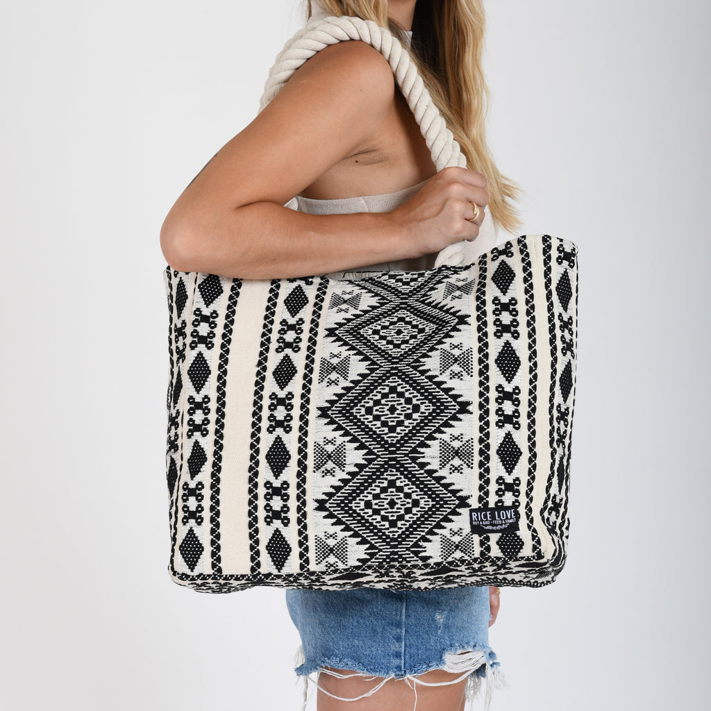 Person holding a black and white patterned tote bag on a plain background