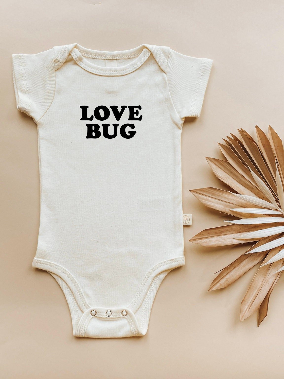 White baby onesie with 'LOVE BUG' text on a beige background
