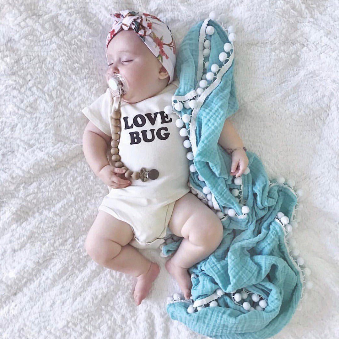 Baby wearing a 'Love Bug' onesie with a turquoise blanket and beads on a white textured surface