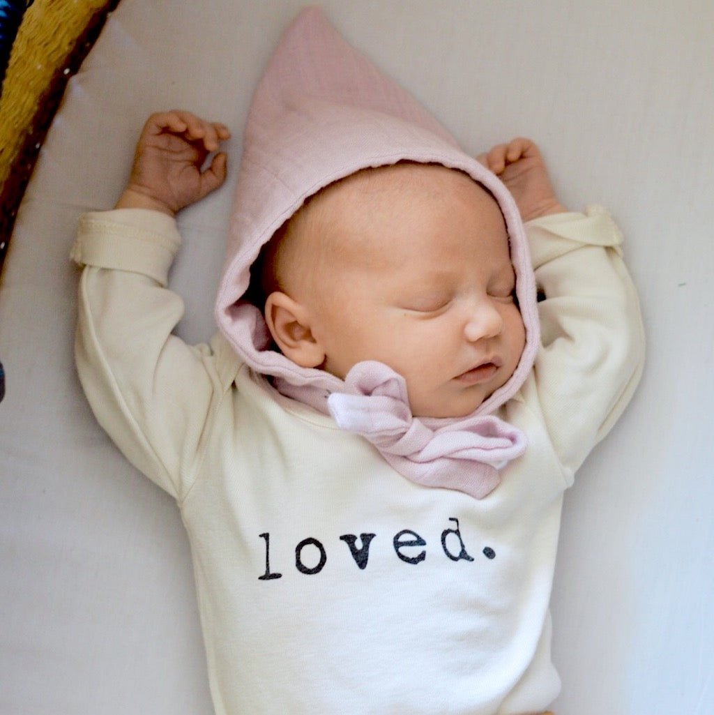 Newborn baby wearing a pink hooded outfit with 'loved.' text on a white background