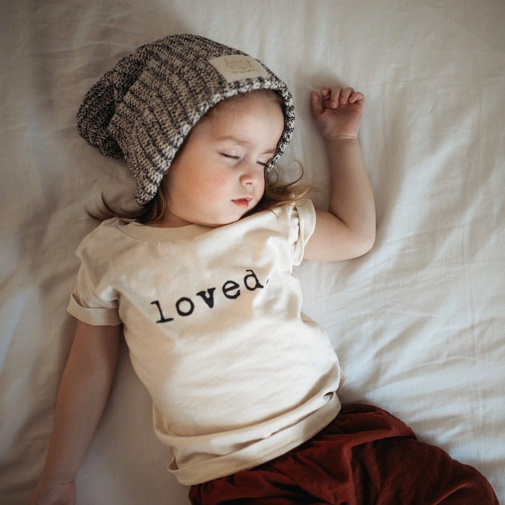 Child wearing a knit hat and 'loved' t-shirt lying on a white blanket