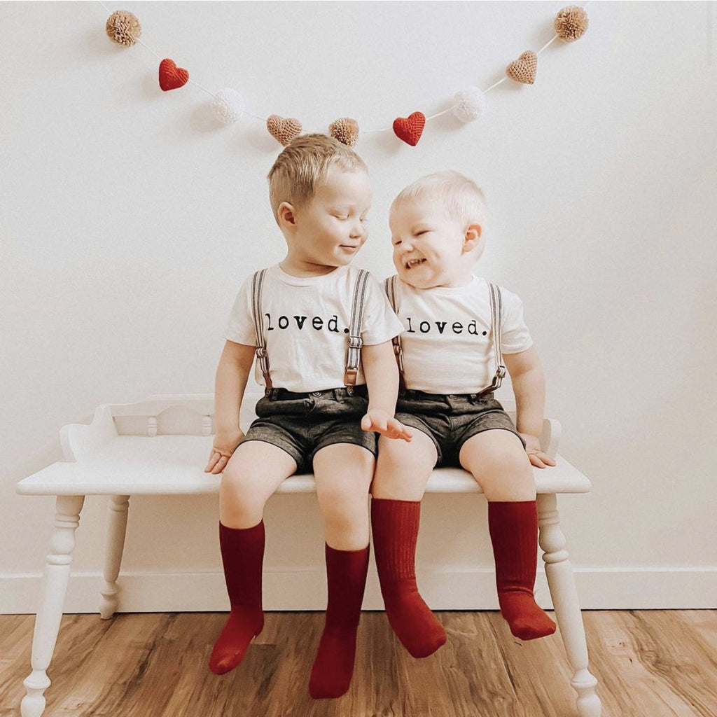 Two children sitting on a bench wearing matching outfits with the word 'loved' and red socks.