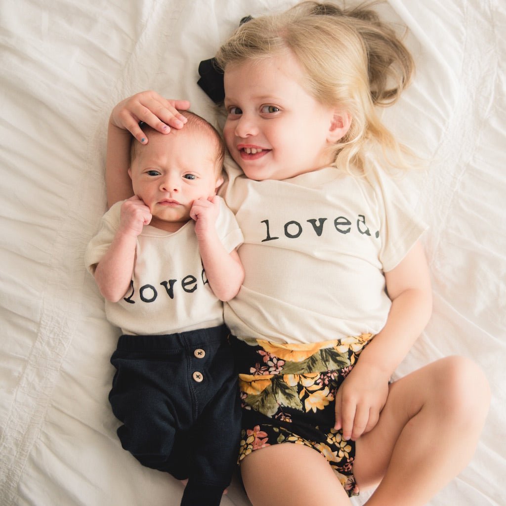 Two children wearing 'loved' shirts lying on a white surface.