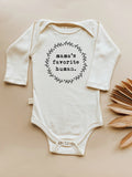 White baby onesie with 'mama's favorite human' text on a beige background