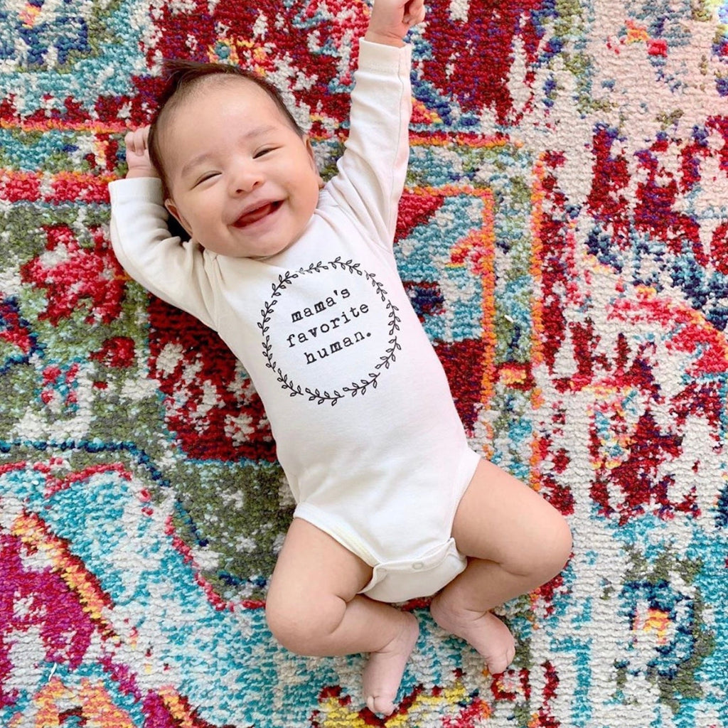 Baby wearing a onesie with 'mom's favorite human' text on a colorful rug